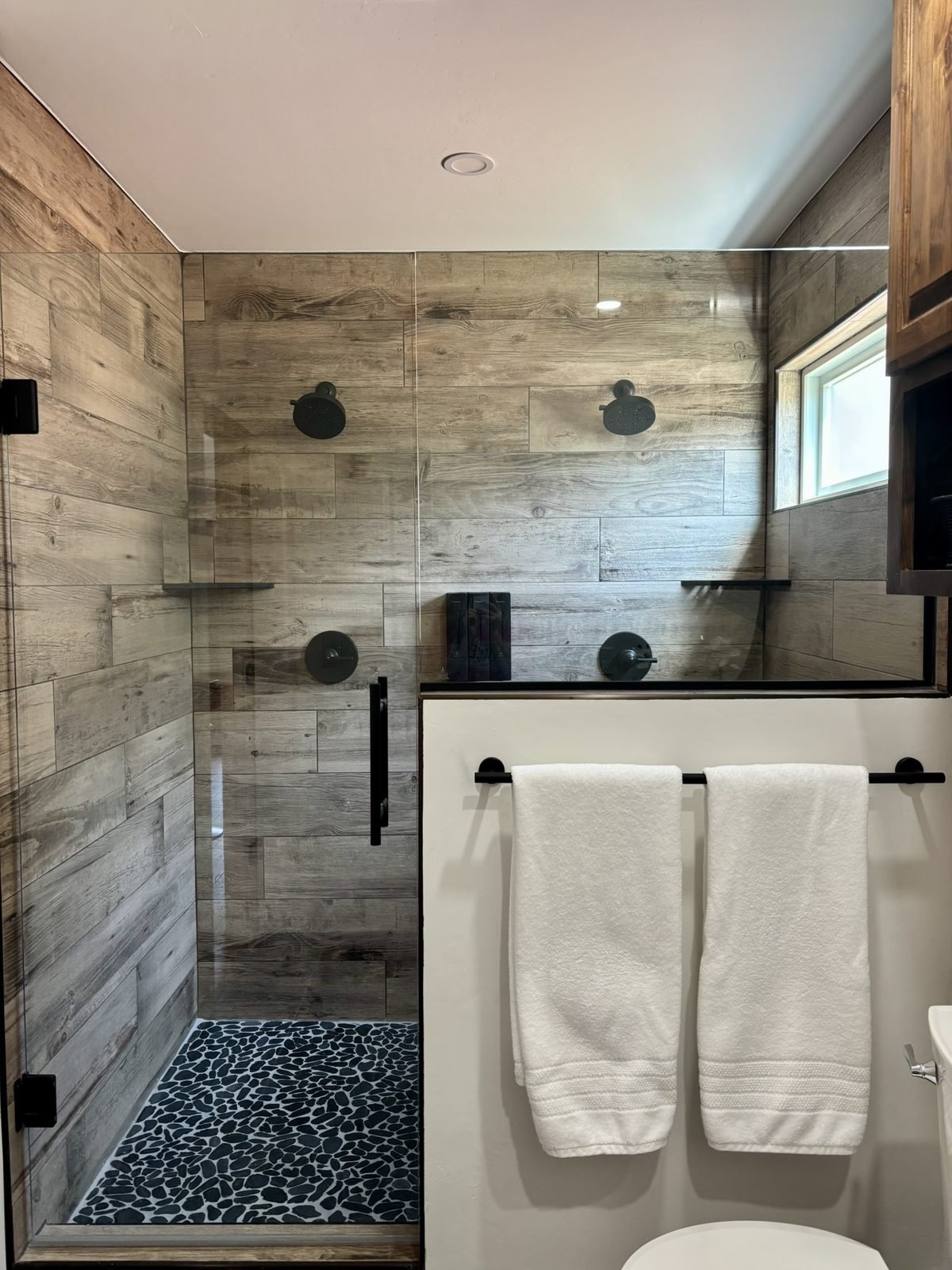 The walk-in shower with two showerheads, wood-look tile and a pebble floor