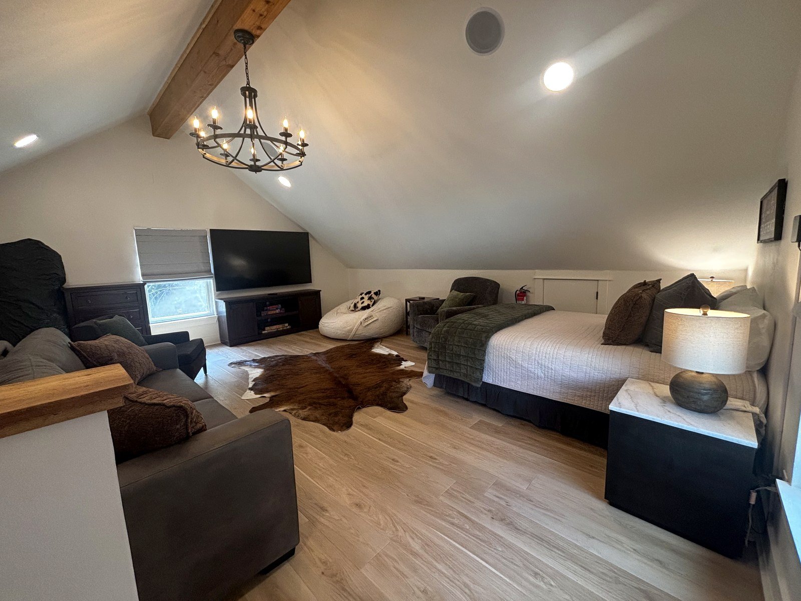 The other end of the loft, with the 75-inch television above a wooden console, a dresser, seating and the bed to the right