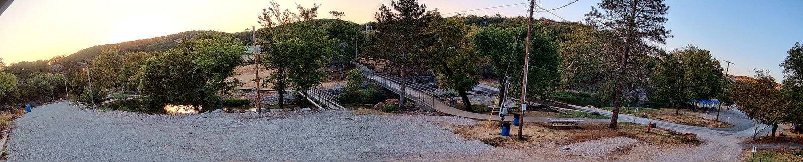 The park at sunrise seen from the cabin: the gravel clearing, Honey Creek and two footbridges, and first light coming over the Arbuckle hills