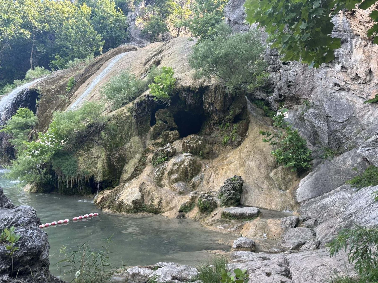 A cave mouth in the rock beside water in Turner Falls Park