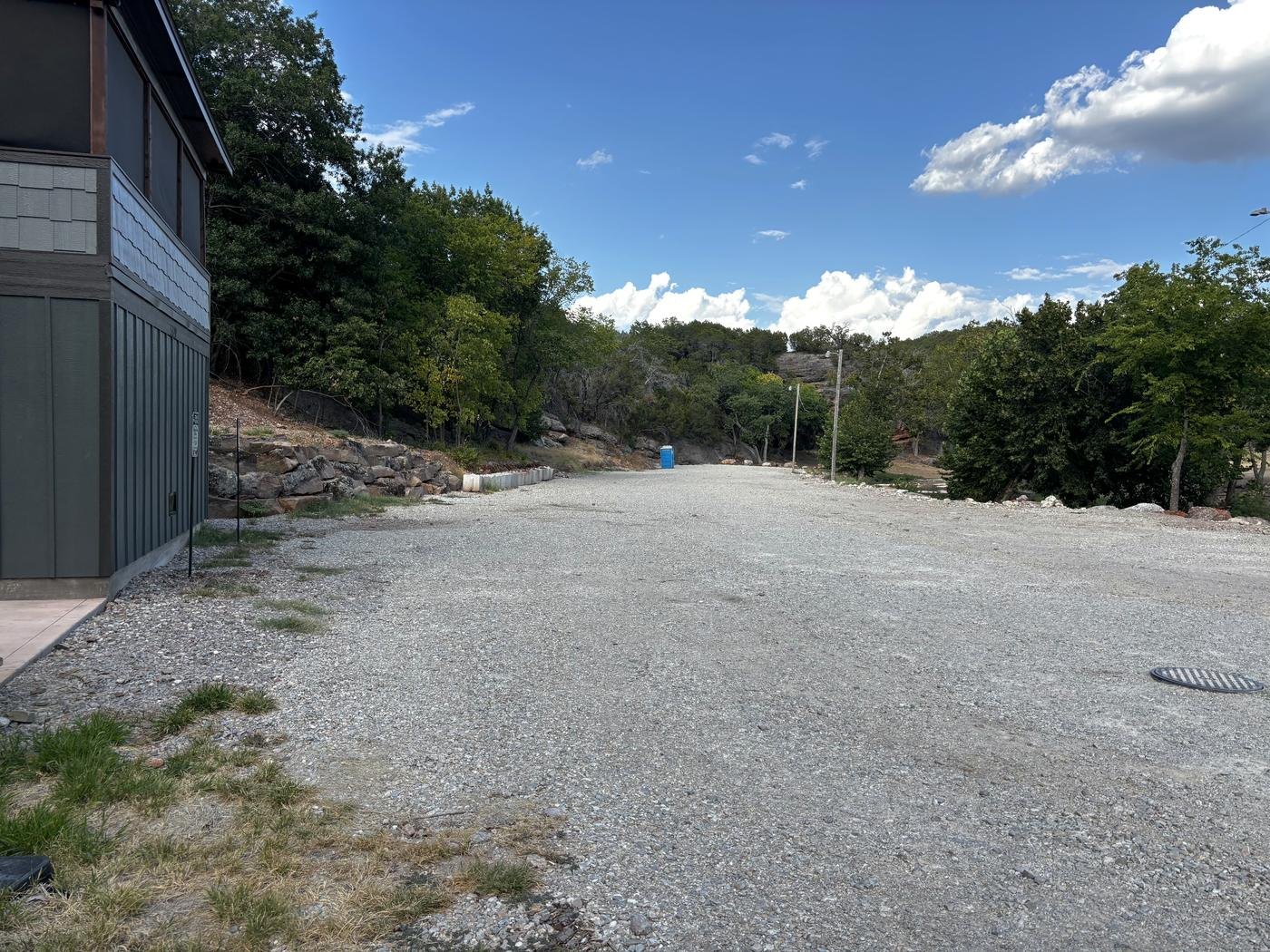 The wide gravel lot beside the cabin, empty, with the Arbuckle hills beyond